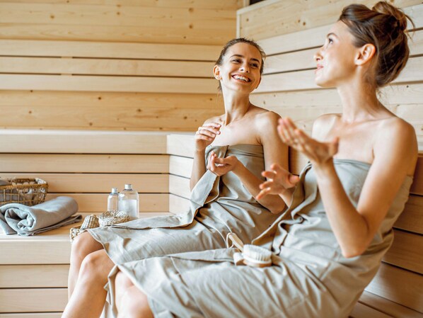 Two individuals in a sauna setting with wooden benches and towels.