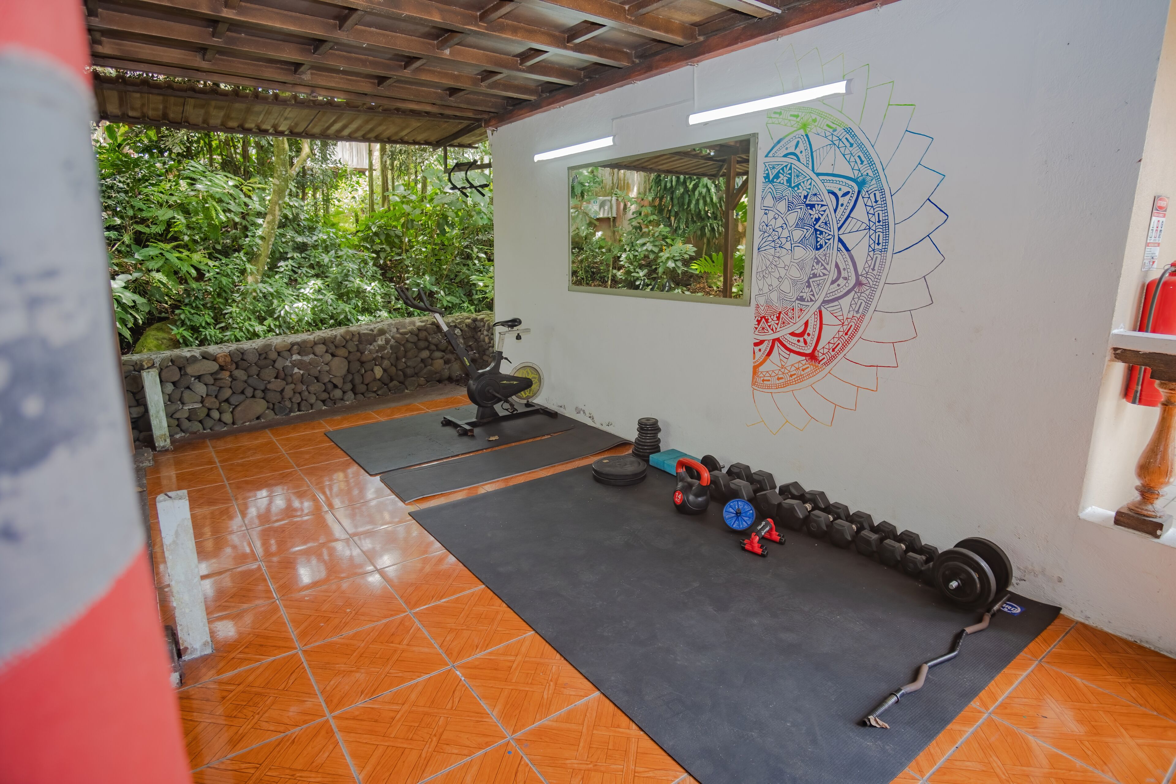 Un gimnasio con equipo de ejercicio, una pared de piedra y una ventana con vistas a la vegetación.