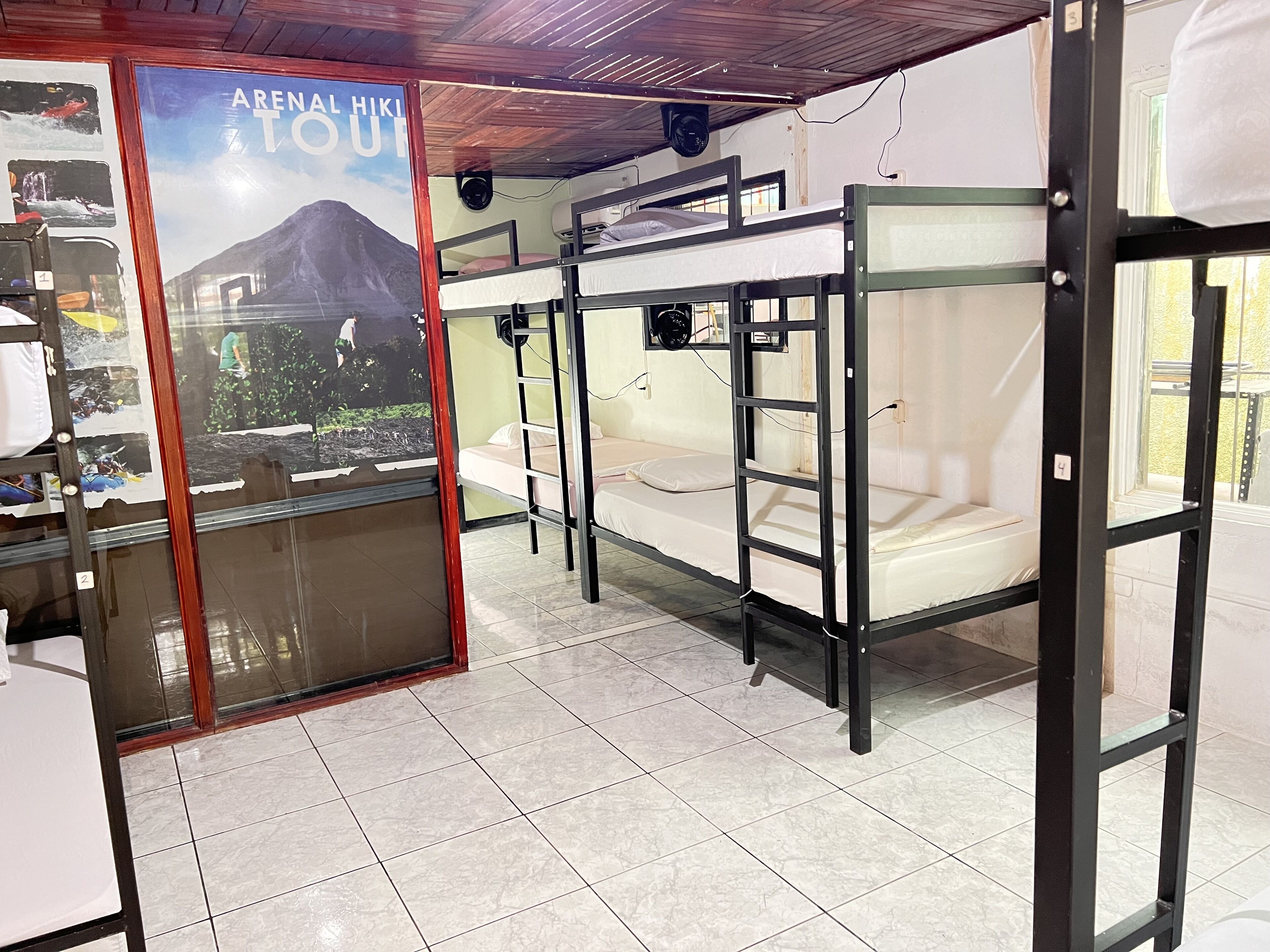 A room with bunk beds, a poster advertising a hiking tour, and a tiled floor.