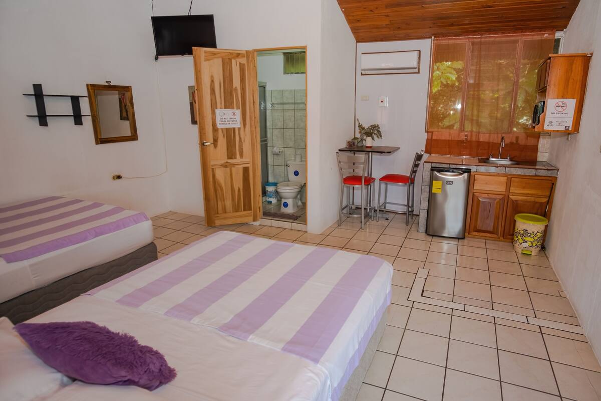 Une chambre avec deux lits, une petite kitchenette, un espace douche et un plafond en bois.