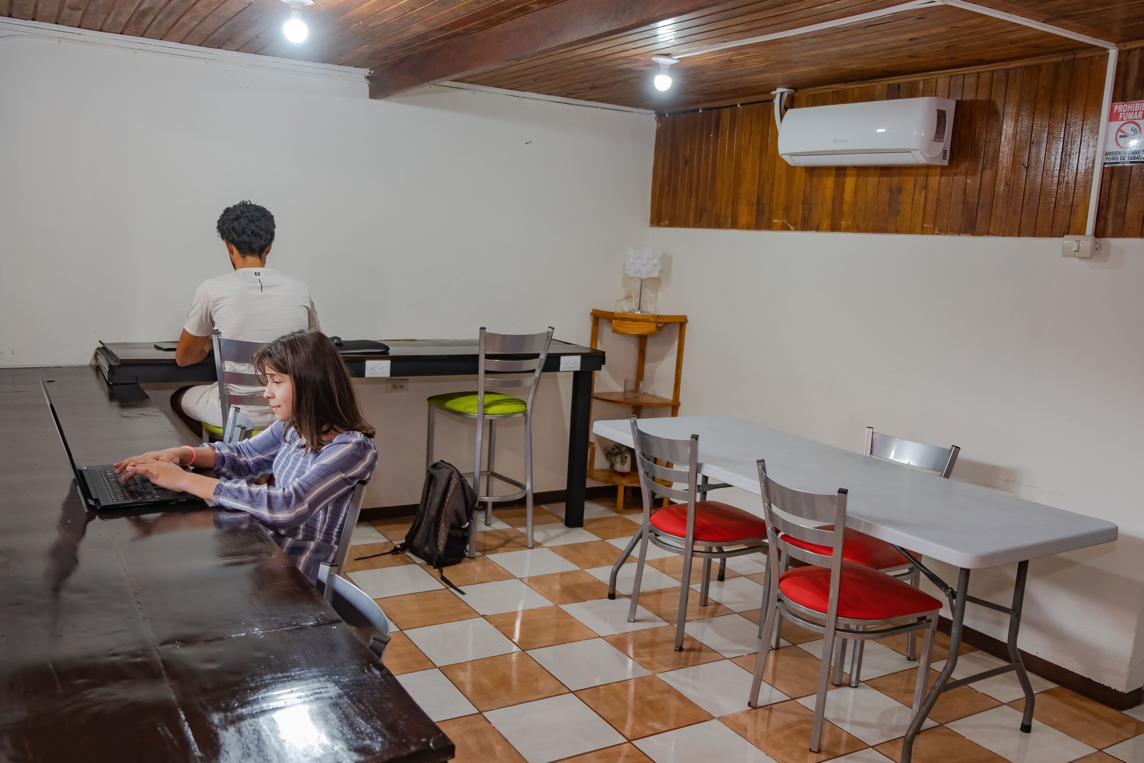 Una habitación con una mesa larga, sillas y una persona usando una computadora portátil.