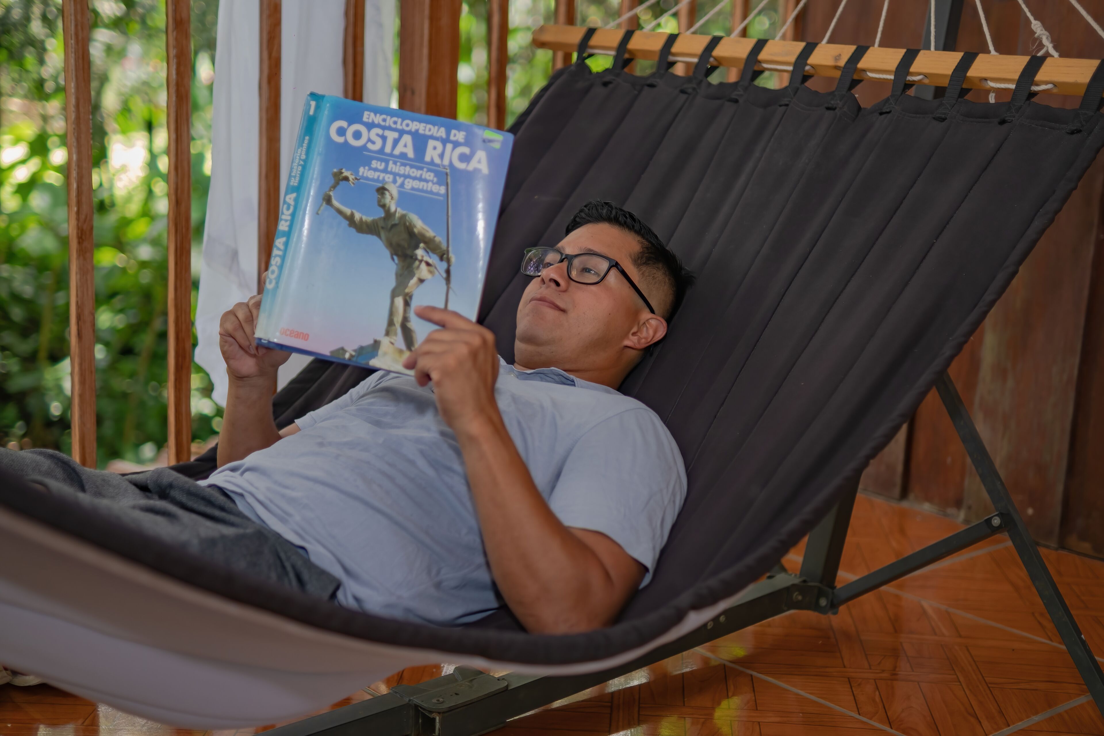 A person lying in a hammock reading a book titled 'Encyclopedia de Costa Rica'.