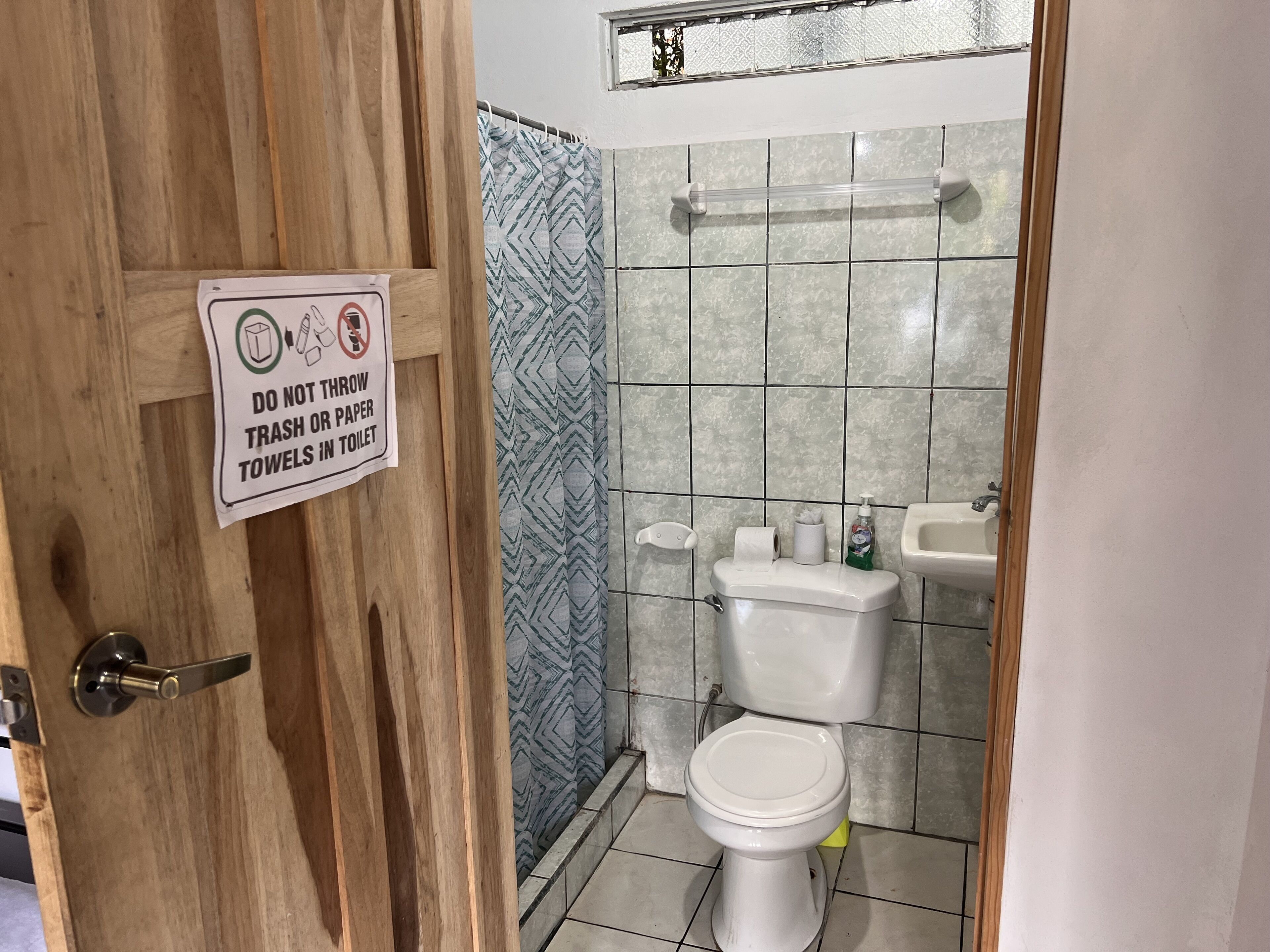 A bathroom with a sign instructing not to throw trash or paper towels in the toilet.