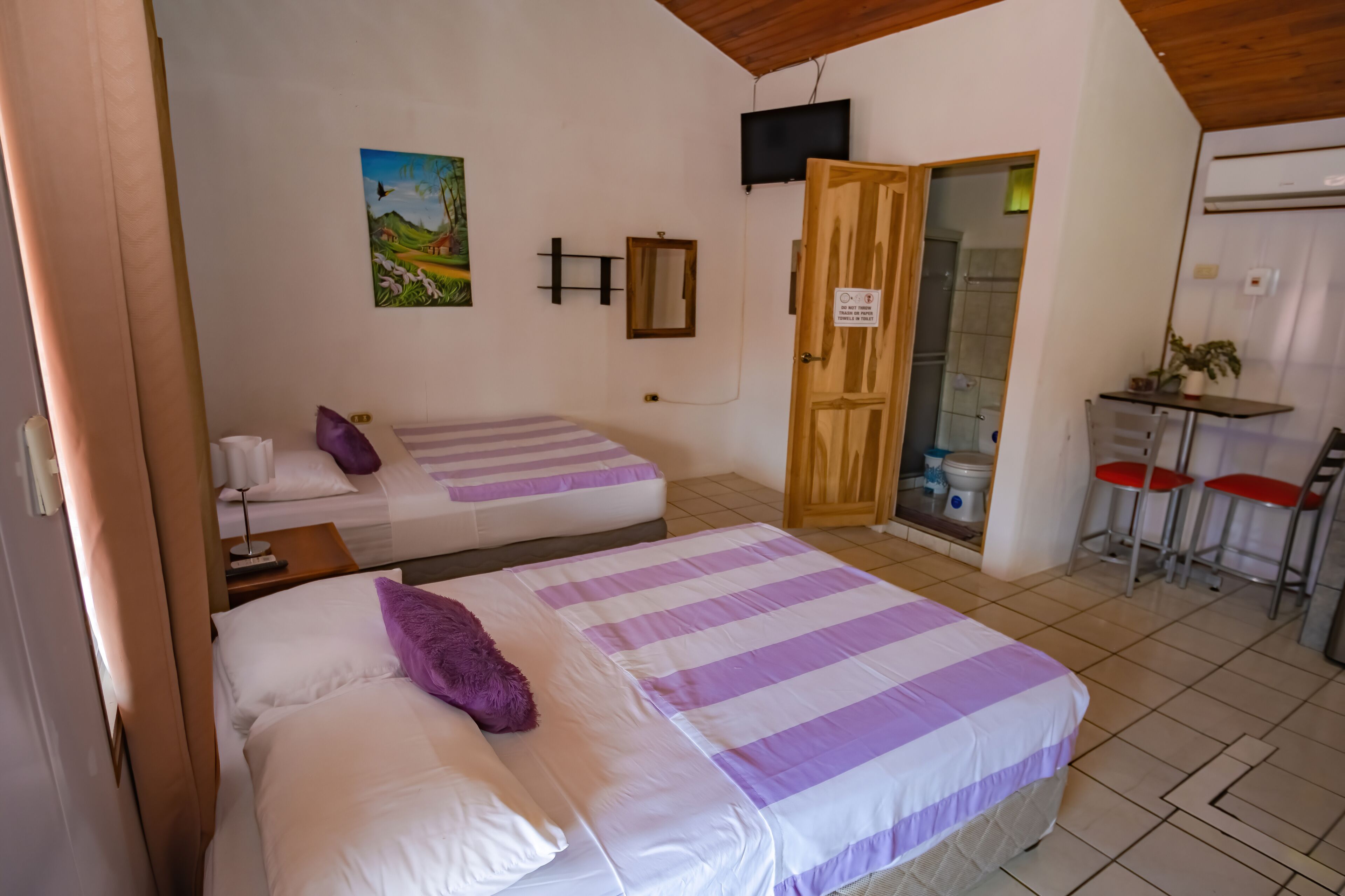 Une chambre avec deux lits, un bureau, une chaise, une télévision et une porte donnant sur une salle de bain.