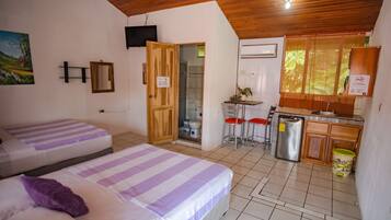 Una habitación con dos camas, techo de madera, una zona de cocina con refrigerador y un baño con ducha.