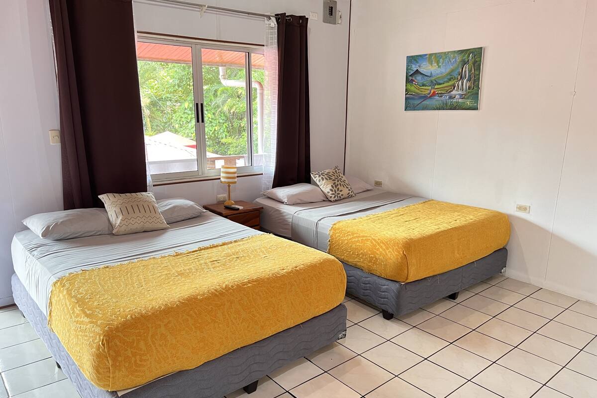 Une chambre avec deux lits, une fenêtre avec des rideaux, un tableau au mur et un sol carrelé.