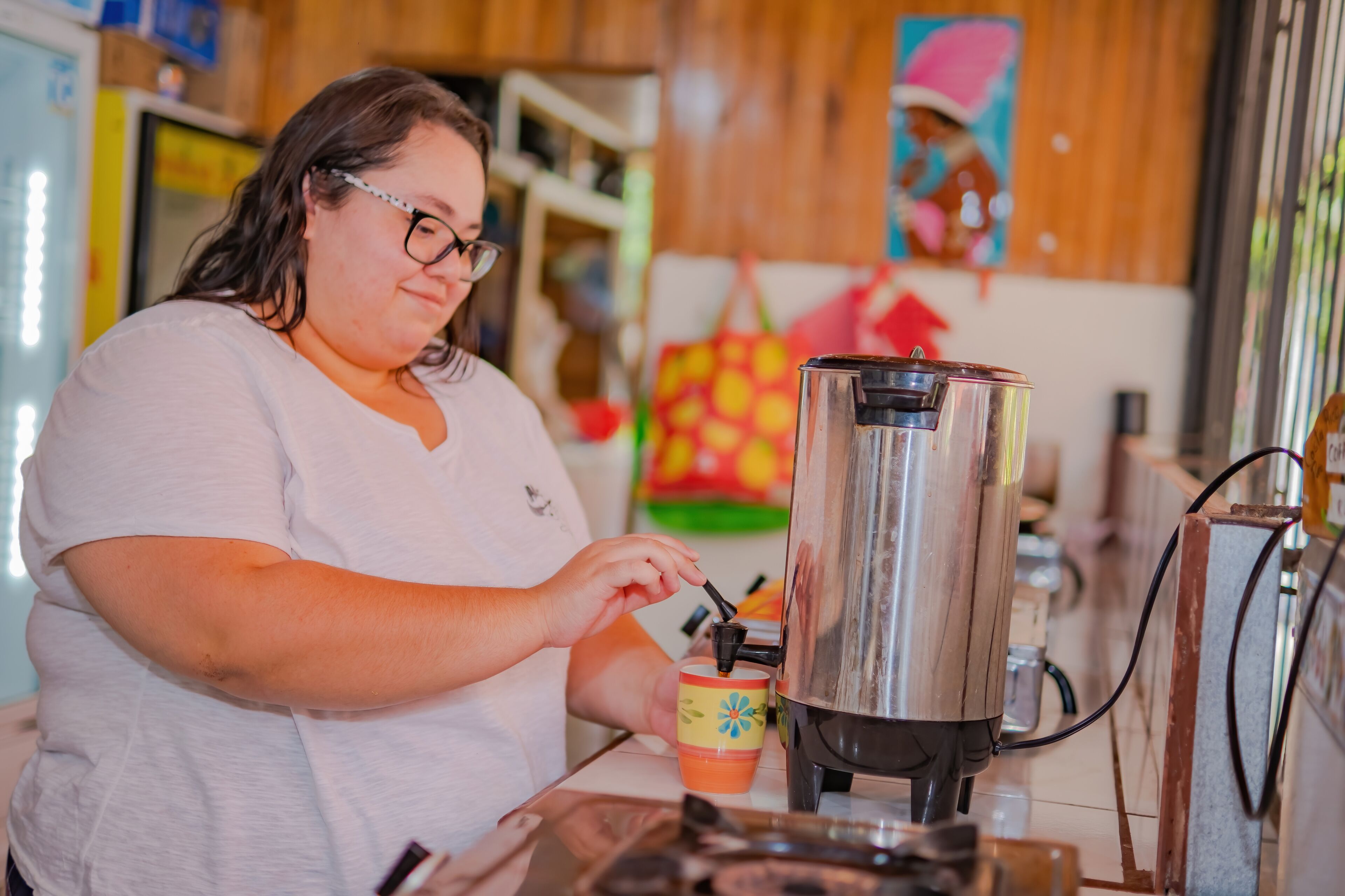 A person operating a coffee machine in a kitchen area with wooden cabinets and a colorful wall decoration.