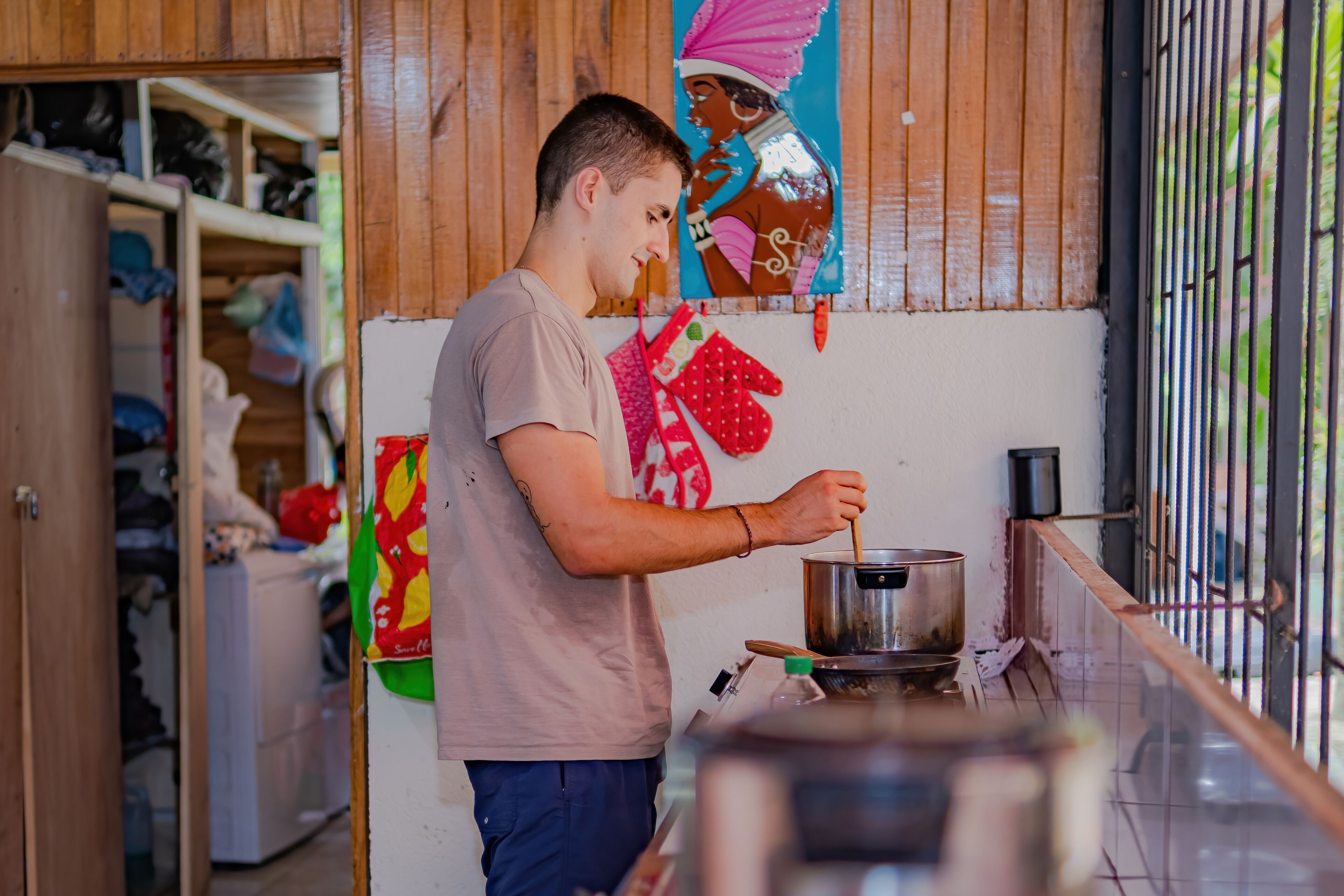 A person cooking in a kitchen with wooden cabinets and a mural on the wall.