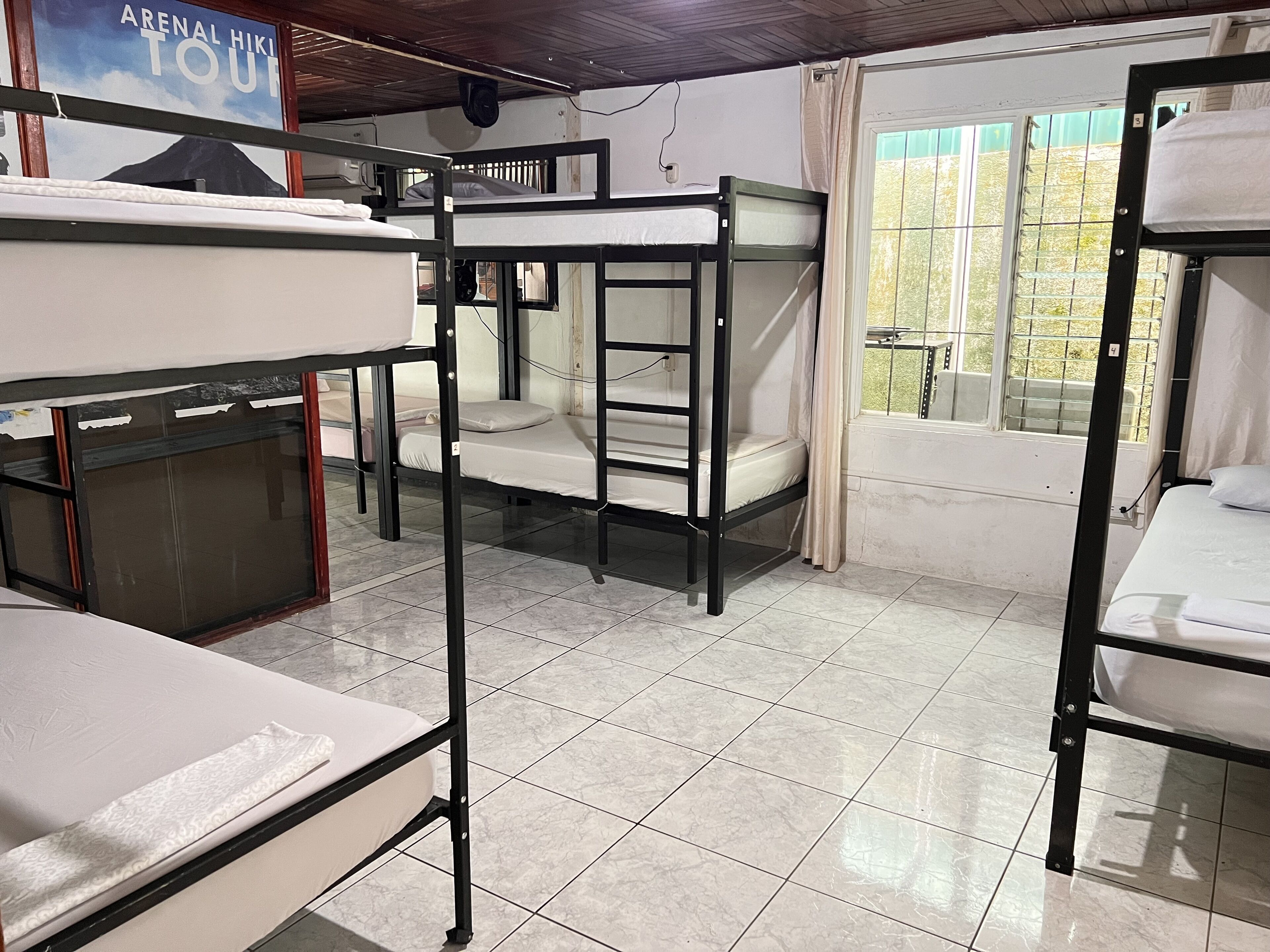 Un dormitorio con literas, suelo de baldosas, ventana con vistas y un cartel en la pared.