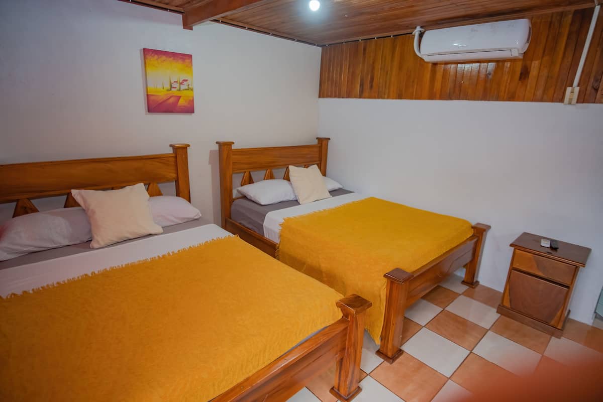 Une chambre avec deux lits en bois, une petite table de chevet en bois et un ventilateur de plafond.