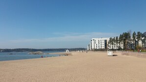 A sandy beach with a clear sky, a few people, and a building with multiple floors in the background. - Nice apartment with sea view<br> (Helsinki)