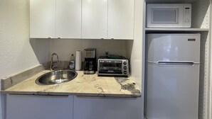 A compact kitchen with white cabinets, a stainless steel sink, a microwave, and a built-in refrigerator.