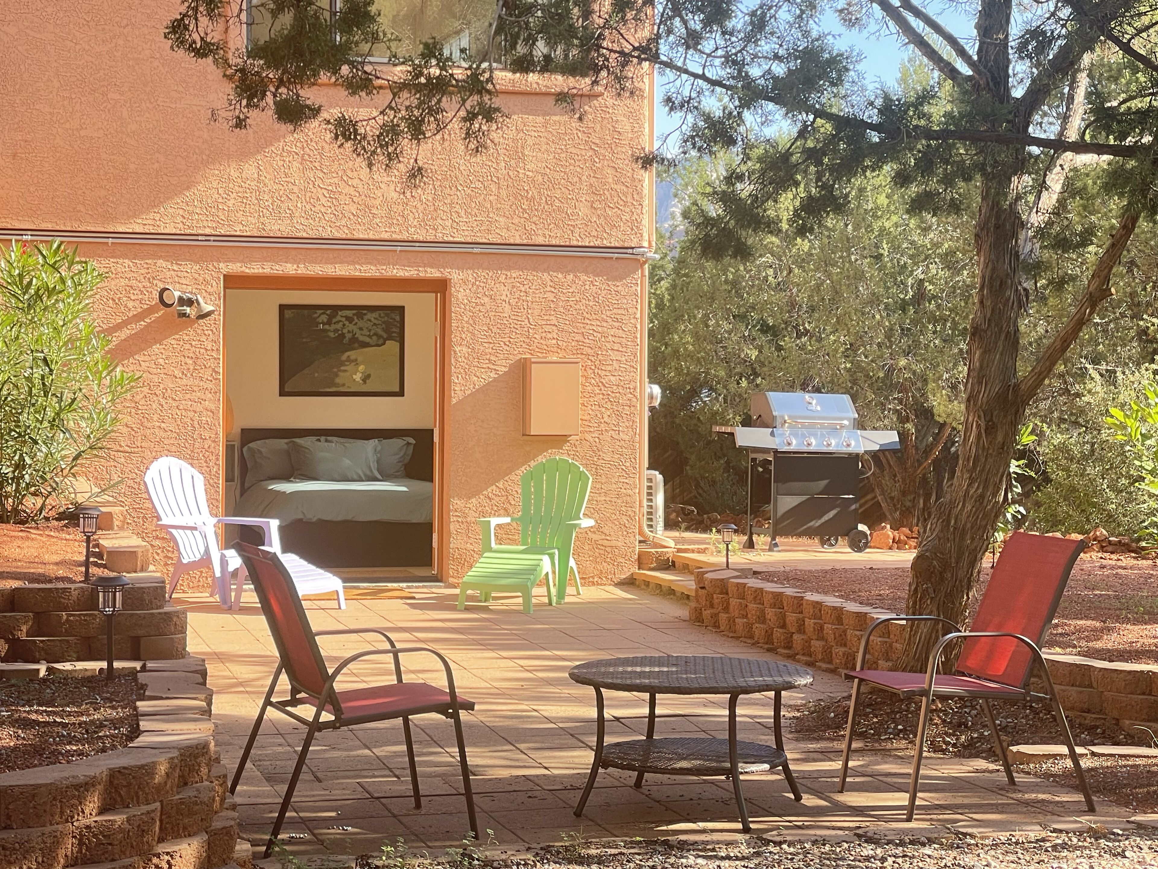 Een terras met buitenmeubilair, een barbecue en een bed zichtbaar door een open deur.