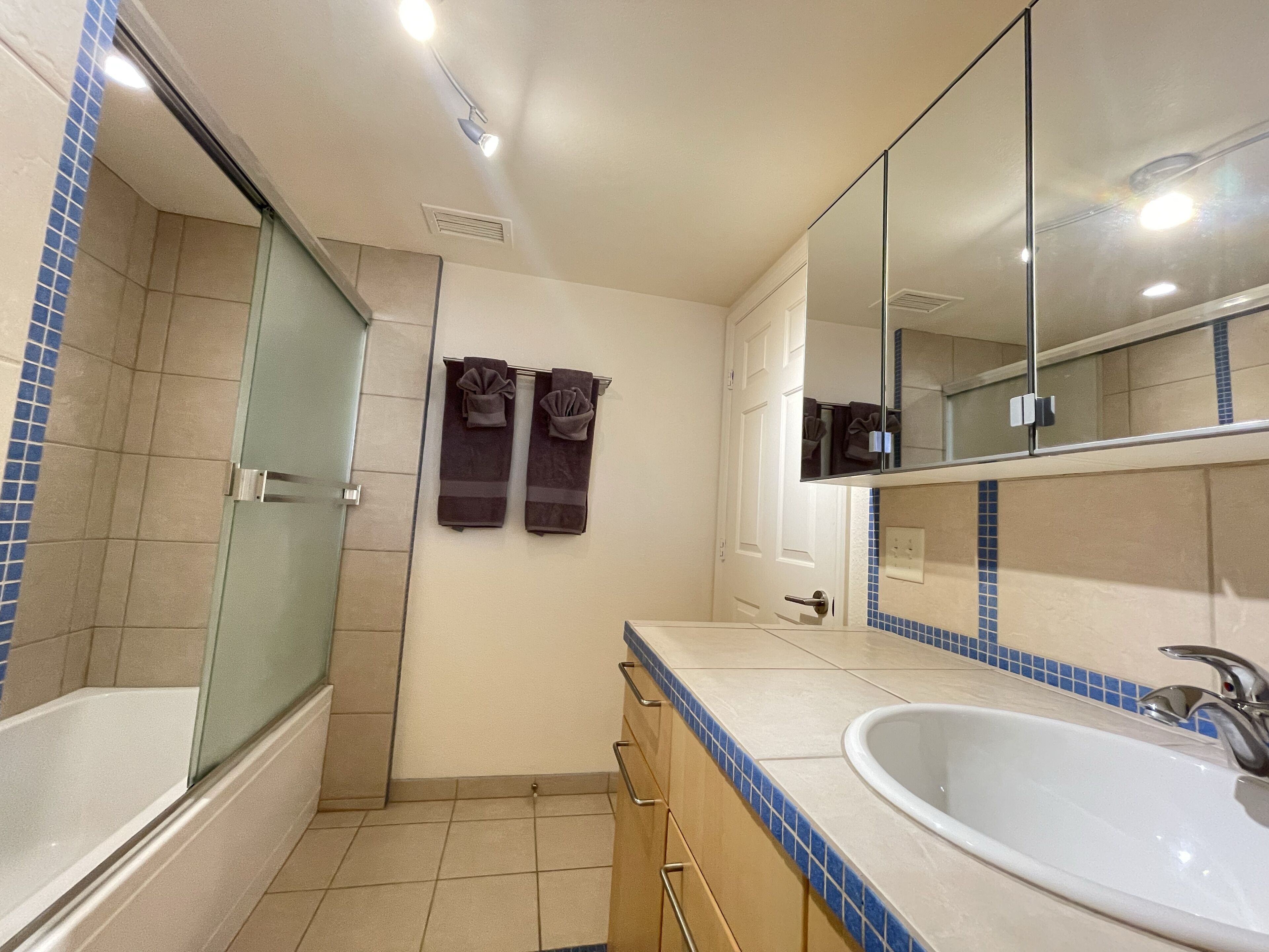 A bathroom with a bathtub, a sink, a mirror, and towels hanging on the wall.