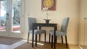A room with a sliding glass door leading to an outdoor area, a small table with two chairs, a potted plant, and a colorful abstract painting on the wall.