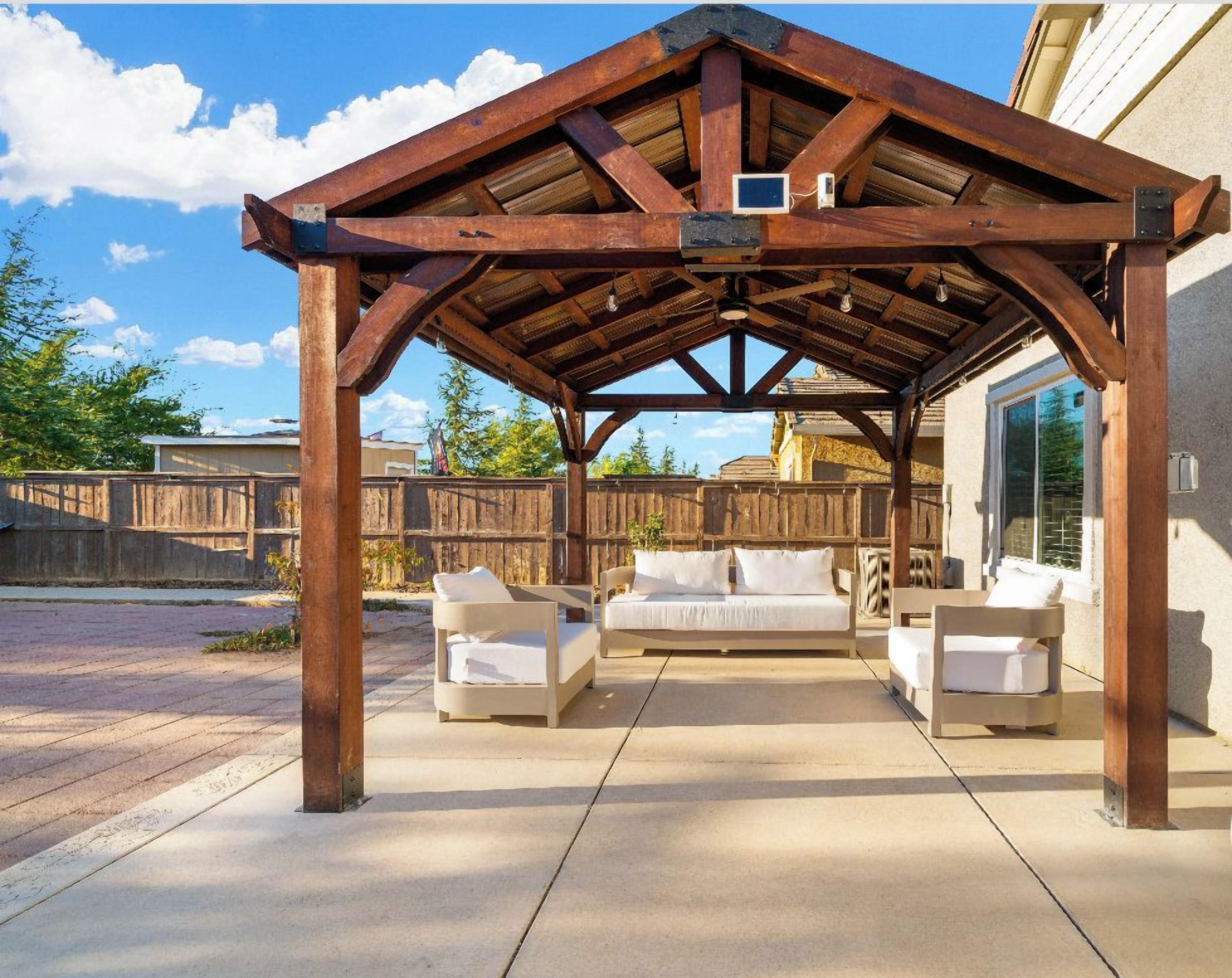 Eine überdachte Terrasse mit einer Holz-Pergola, weißen Sitzmöbeln mit Auflagen und einem Betonboden.