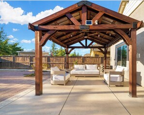 A covered patio with a wooden pergola, white cushioned seating, and a concrete floor. - cheerful 4 bedroom with beautyfull back yard (Elk Grove)