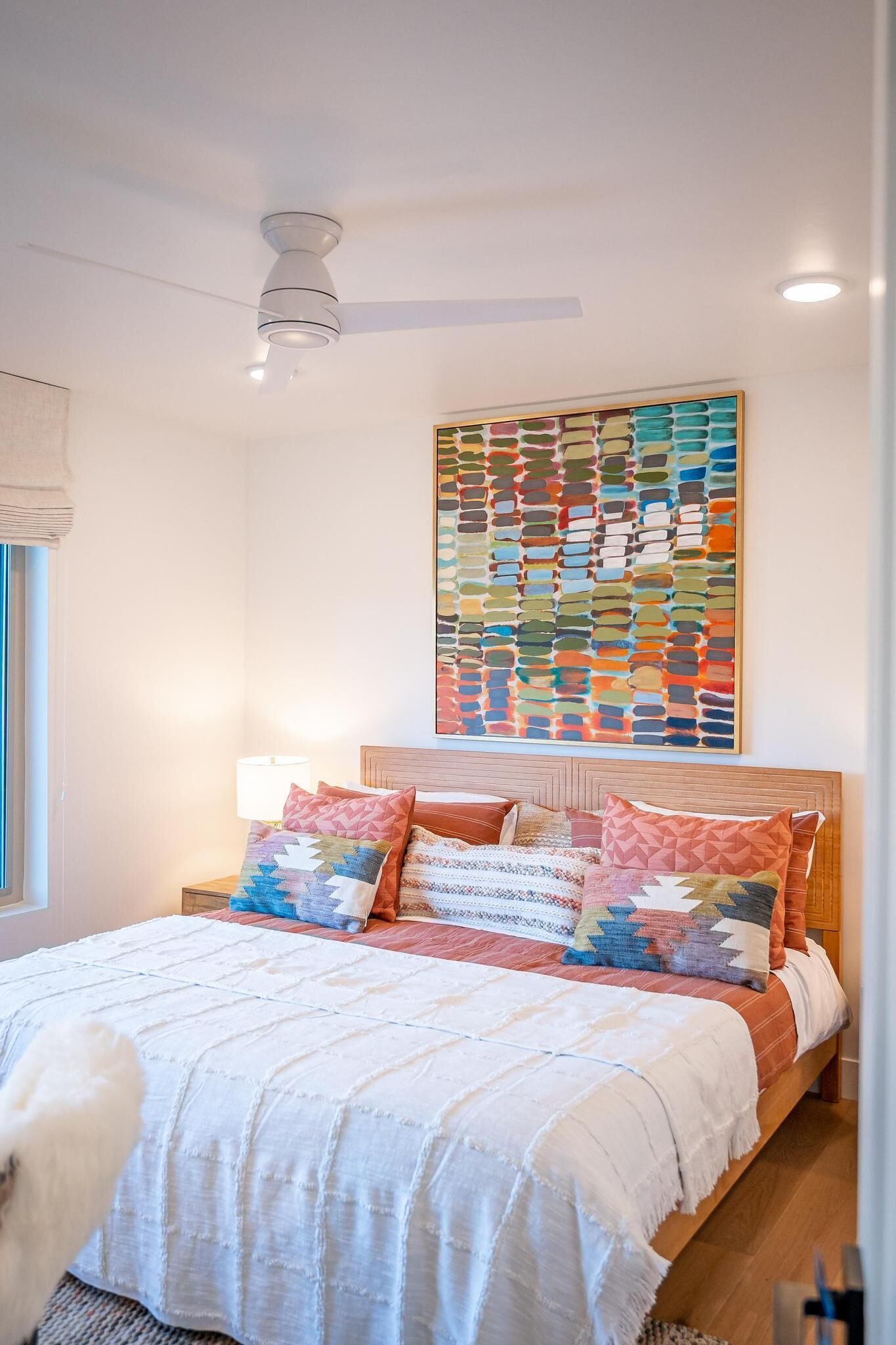 A bedroom with a bed, pillows, a headboard, a ceiling fan, and a wall art piece.