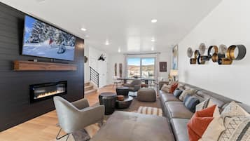 Uma sala de estar moderna com lareira, assentos confortáveis, uma área de jantar e uma televisão grande exibindo uma paisagem nevada.