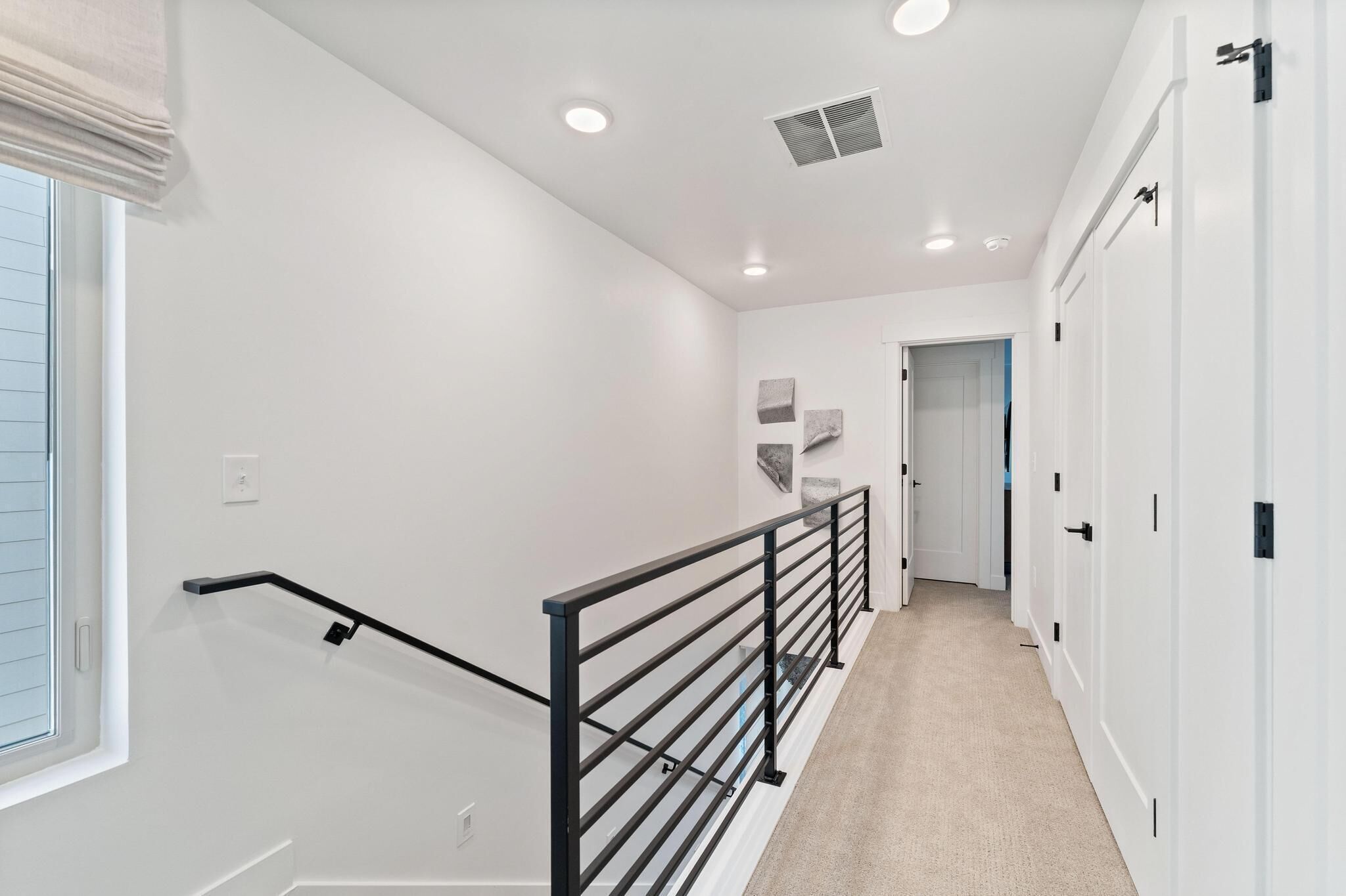 A hallway with white walls, a black railing, and a carpeted floor.
