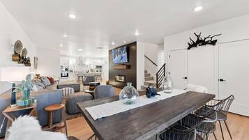 Uma sala de estar moderna com uma mesa de jantar de madeira, assentos confortáveis e uma TV fixada na parede.