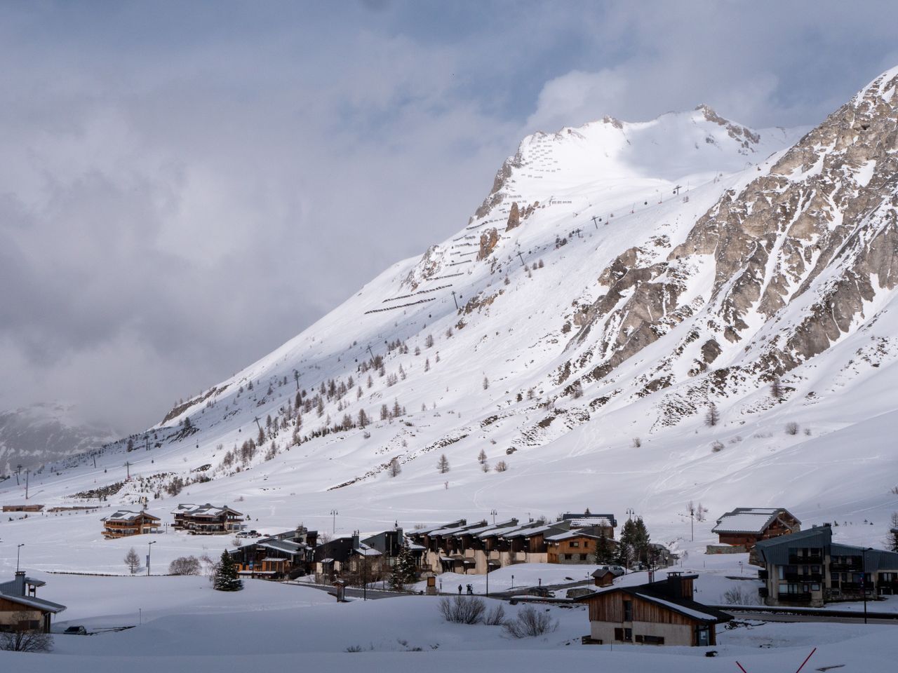 Ein verschneites Bergdorf mit Häusern und einer Skipiste.