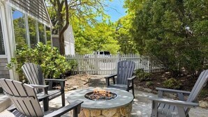 A patio with Adirondack chairs, a stone fire pit, and a white picket fence.