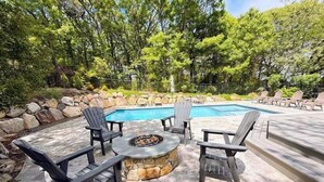 An outdoor pool area with a fire pit, lounge chairs, and a stone fire table.
