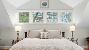 A bedroom with a large bed, two bedside lamps, and a window with a view of trees.