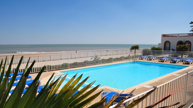 Une piscine avec des chaises longues bleues et vue sur la plage.