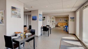 Un espace de restauration moderne dans un hôtel, avec une longue table, des chaises et des œuvres d’art accrochées aux murs.
