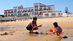 Une plage de sable avec, en arrière-plan, un grand bâtiment blanc agrémenté de touches de rouge.