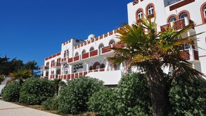 Un bâtiment blanc agrémenté de touches de rouge et doté de nombreux balcons, entouré de verdure.