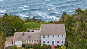 Una casa de dos pisos con garaje, rodeada de vegetación y con vistas al mar.