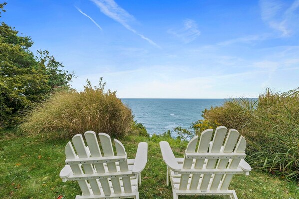 Two white Adirondack chairs facing a body of water with a clear sky. - Stunning Oceanview: Walk to Private Beach (Plymouth)