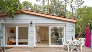 Ein kleines, eingeschossiges Haus mit einer Terrasse und bodentiefen Fenstern, die in ein Schlafzimmer und ein Wohnzimmer führen.