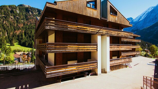 A modern wooden building with multiple balconies, set against a mountainous backdrop. - Cosy apartment for 5 guests with WIFI, hot tub and TV (Canazei)