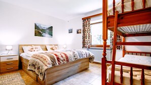 Et soveværelse med en træseng, et natbord, en kommode, en radiator og et vindue med gardiner.