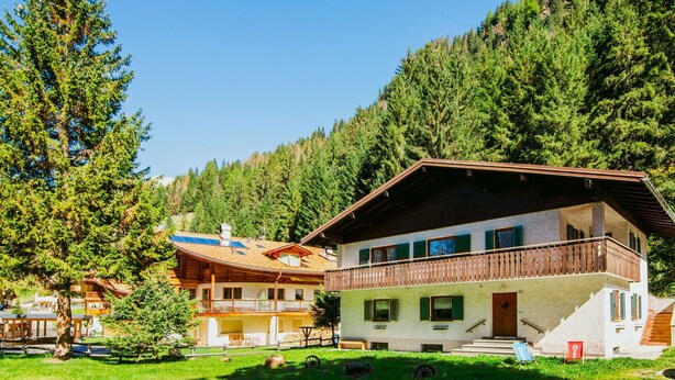 En toetagers chalet med balkon, omgivet af et skovklædt bjerglandskab.