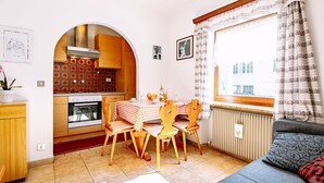 Un espai vital compacte amb cuina, zona de dinar i un racó d'ambient agradable vora una finestra.