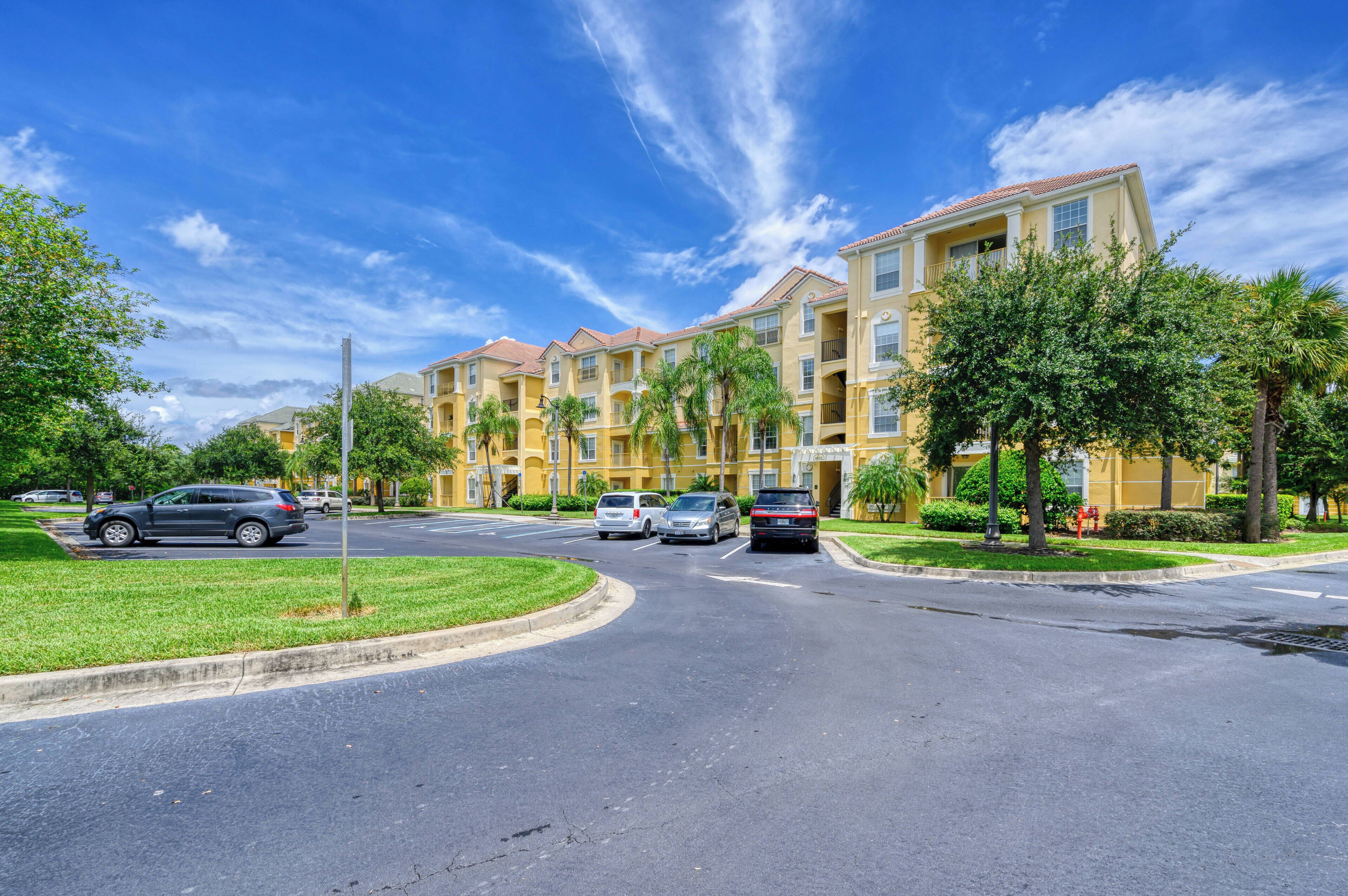 A multi-story residential building with a central courtyard, surrounded by greenery and parked cars.