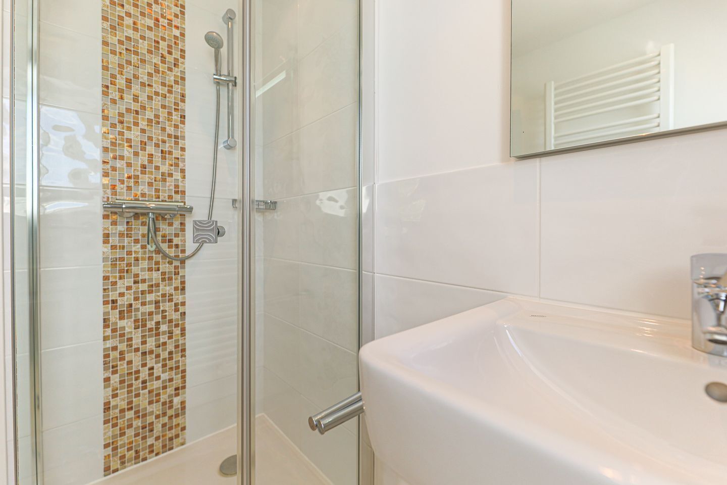A bathroom with a glass shower enclosure, a tiled wall, and a white sink.