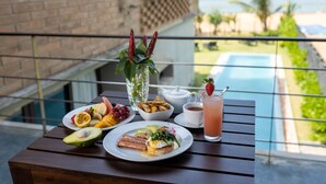 Une table à manger avec des aliments pour le petit-déjeuner, un verre et une vue sur la piscine et l’océan.