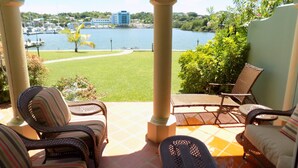 Un patio con muebles de mimbre, vista a un lago y un edificio al fondo.