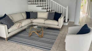 Una sala de estar con un sofá modular, una mesa de centro de vidrio, un sillón blanco y una escalera.