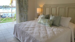 A bedroom with a large bed, a nightstand with a lamp, and a view of a marina through a sliding door. - Bay View #7 is a 1-bed, 1-bath waterfront townhouse in a gated community. (Rodney Bay)