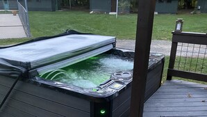 Et spabad med gennemsigtigt låg, omgivet af en træterrasse og et metalhegn.