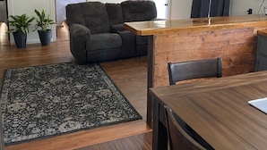 En moderne stue med en sofa, et træsofabord og et spisebord. Der er krukkeplanter og et tæppe på gulvet.