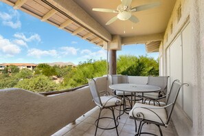 A covered outdoor patio with a table and chairs, a ceiling fan, and a view of a residential area with trees and houses.