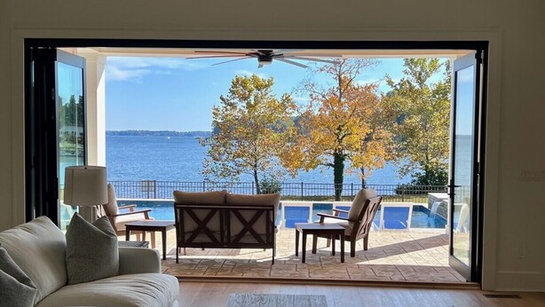 Una habitación con sofá, una mesita de centro y vista a una piscina y árboles a través de una puerta abierta.